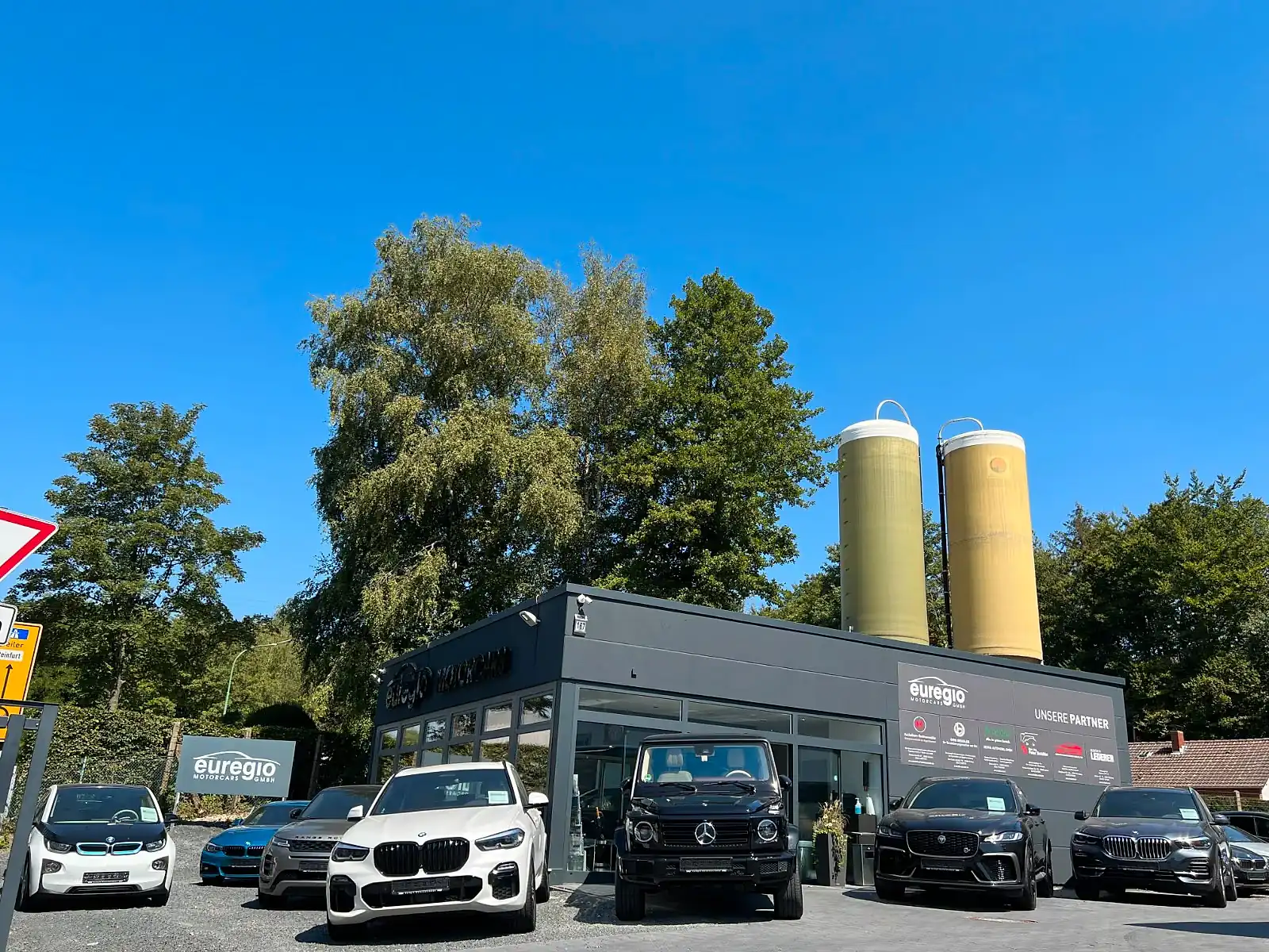 Der Hof von Euregio Motorcars an der Eschweilerstraße: anthrazitfarbene Halle, zwei gelbe Silos, davor die Fahrzeuge
