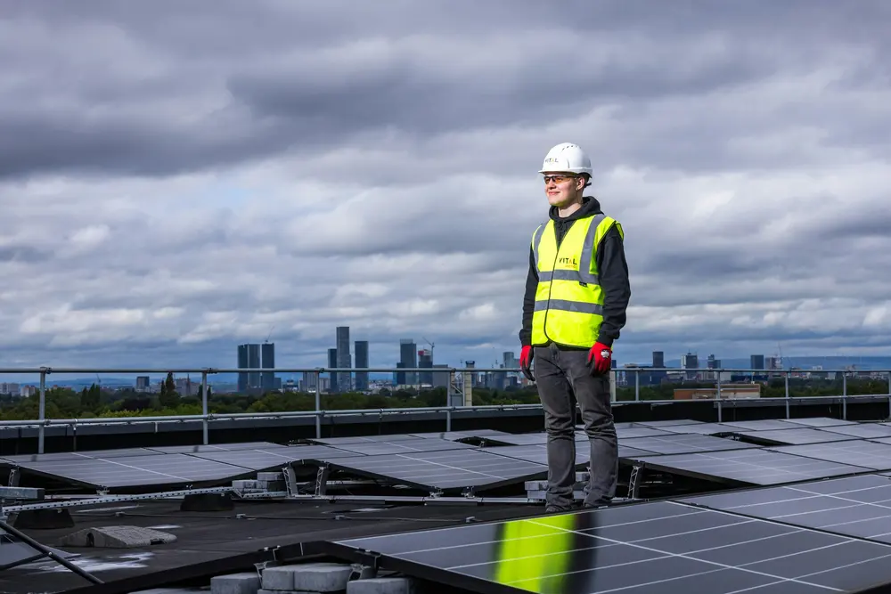 Ingenieur in Warnweste auf einem Dach mit Photovoltaikanlage, im Hintergrund die Skyline