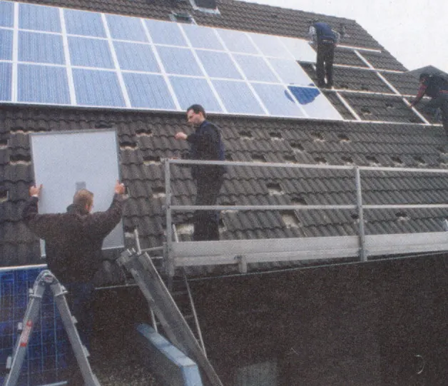 Zwei Monteure tragen ein Solarmodul aufs Dach