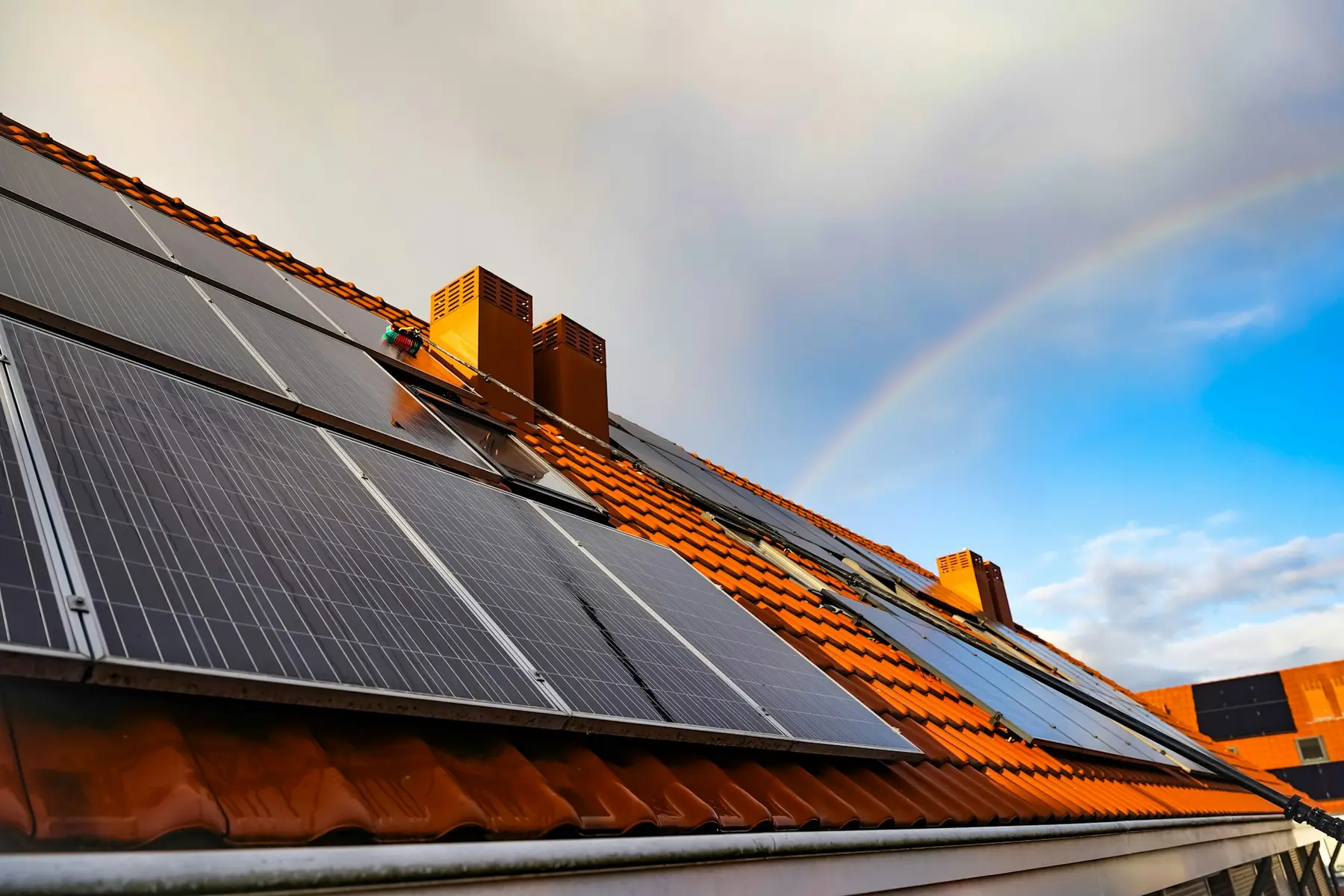 Regenbogen über einem Ziegeldach mit Solarmodulen